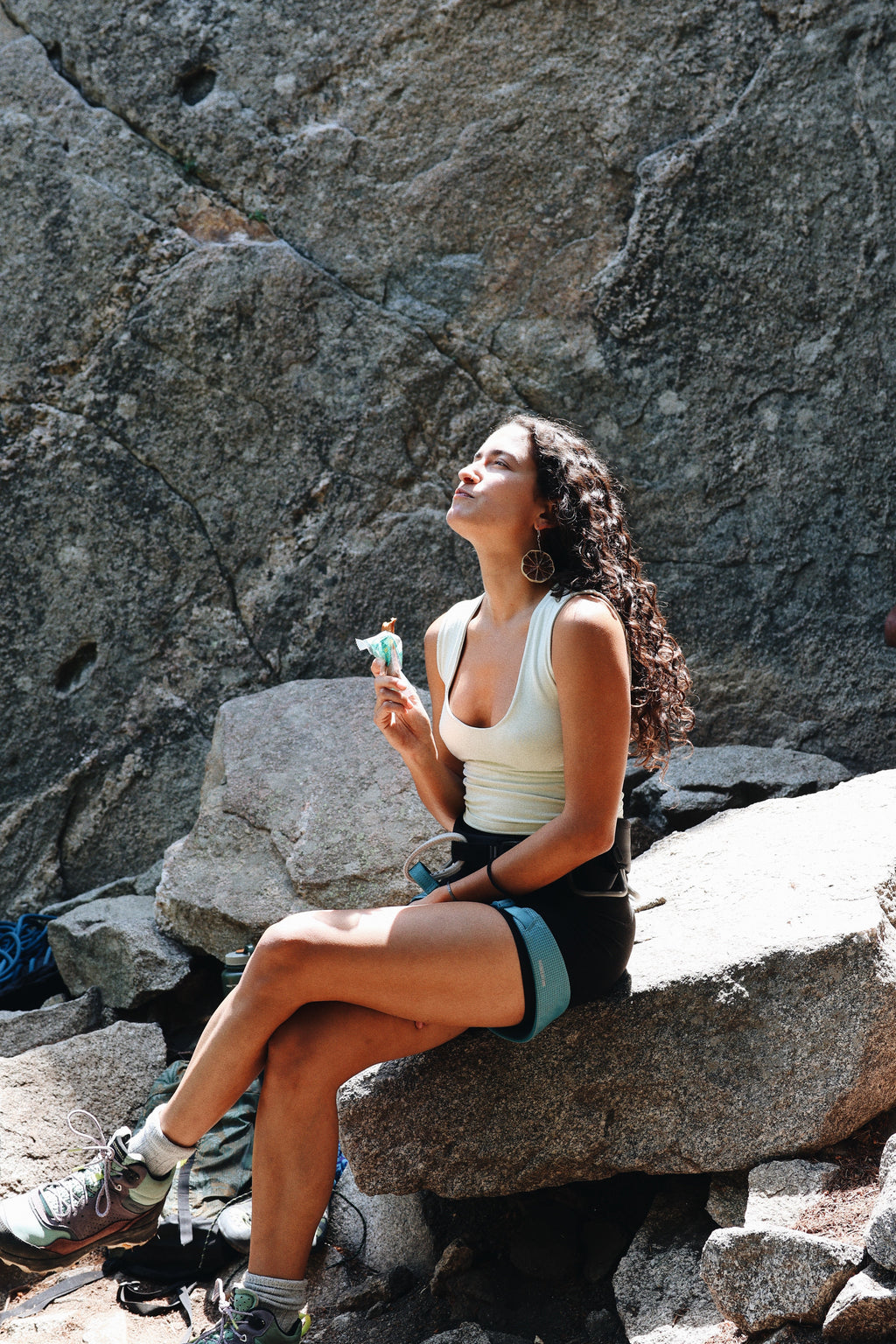 Woman enjoying a South Forty 100% Mango Fruit Bar while resting on a rocky hiking trail, healthy vegan gluten-free one-ingredient dried mango snack, outdoor adventure, natural tropical fruit snack, portable hiking food, wholesome non-GMO fruit bar, scenic mountain break, Product of Ghana & Ivory Coast.
