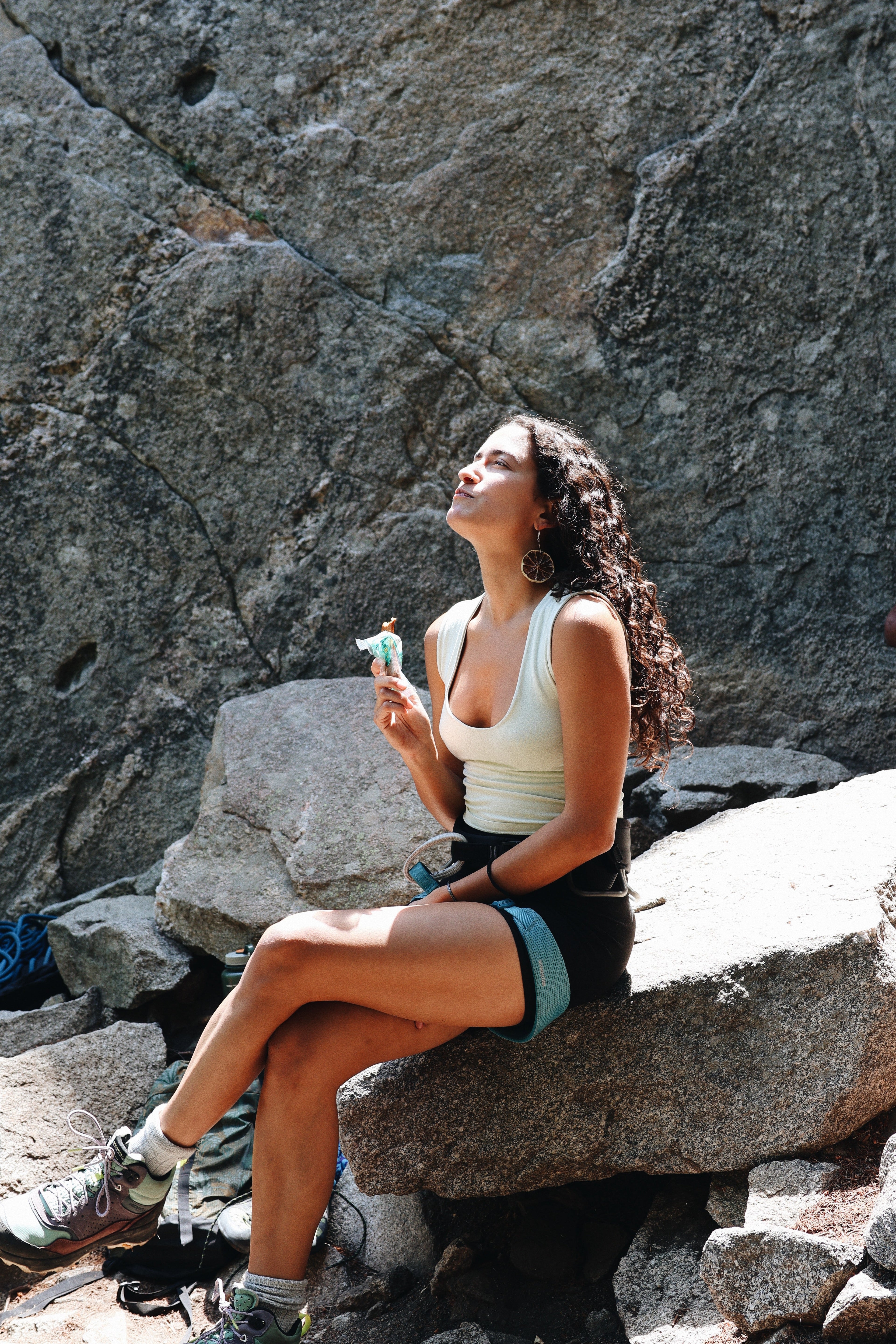 Woman enjoying a South Forty 100% Mango Fruit Bar while resting on a rocky hiking trail, healthy vegan gluten-free one-ingredient dried mango snack, outdoor adventure, natural tropical fruit snack, portable hiking food, wholesome non-GMO fruit bar, scenic mountain break, Product of Ghana & Ivory Coast.