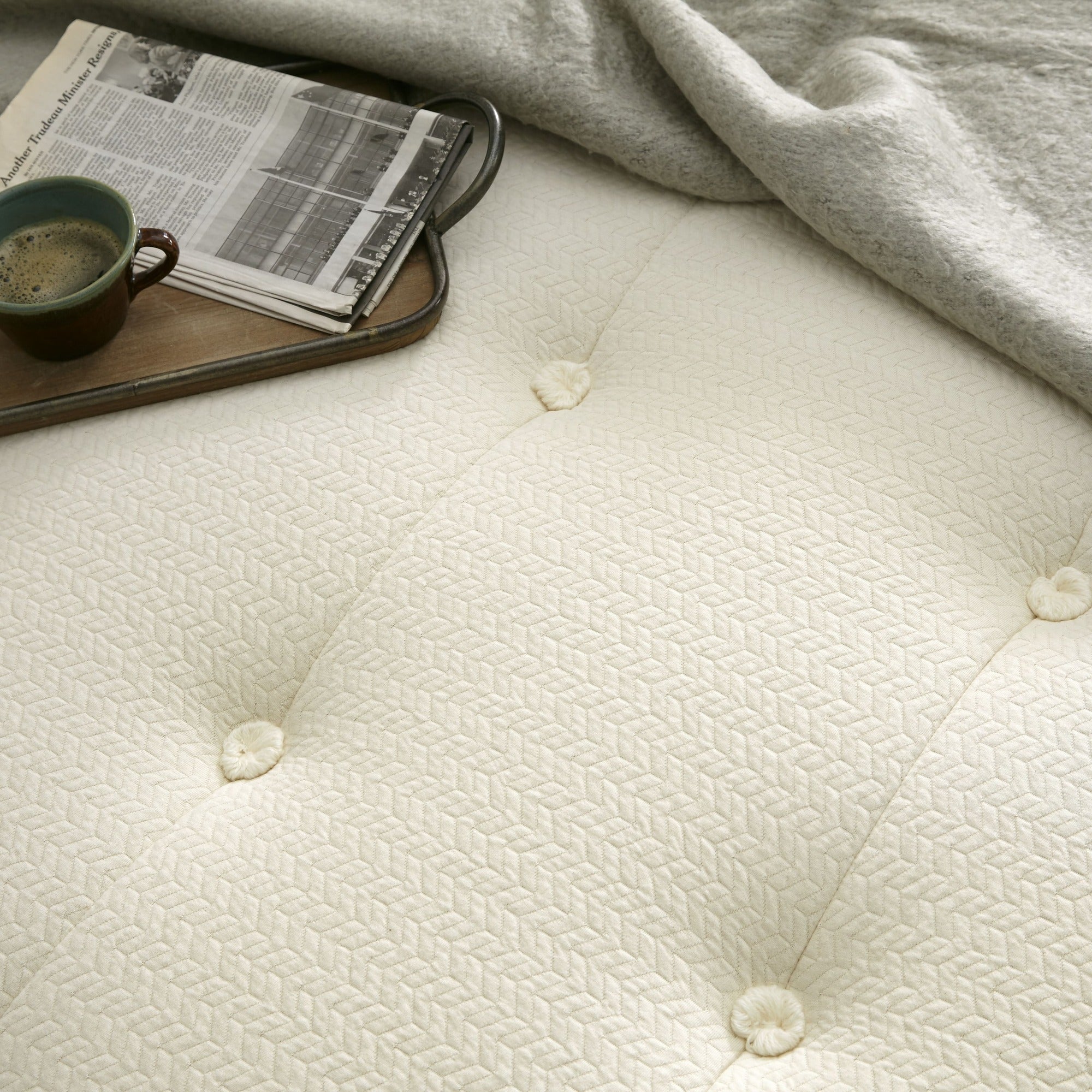 White mattress with a tray holding a cup and newspaper on top, Mattress on a bed in a bedroom with 'Whitney Organics' branding. 100% GOTS & GOLS-Certified organic cotton, wool and latex, 10" profile: 2" organic Dunlop latex + 7-zone pocketed coils, Medium feel for that “just right” balance of comfort + support, Breathable organic wool & cotton cover for airflow and temperature regulation, Lumbar support with zoned coil design, Suitable for an adjustable base & Made with sustainable, renewable materials