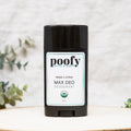 Deodorant stick labeled **Poofy Bath & Body Max Deo Wood & Citrus Deodorant Organic** standing upright on a light neutral background with soft greenery accents.
