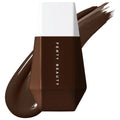 Fenty Beauty Eaze Drop Blurring Skin Tint Foundation bottle in a deep brown shade with a white cap, displayed with a matching foundation swatch on a white background.