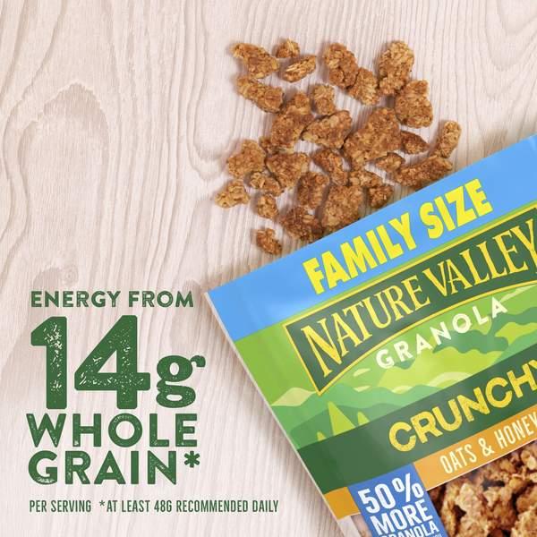 Nature Valley Crunchy Oats & Honey Family Size Granola package with crunchy granola clusters scattered on a light wood surface, highlighting 14g whole grain per serving.