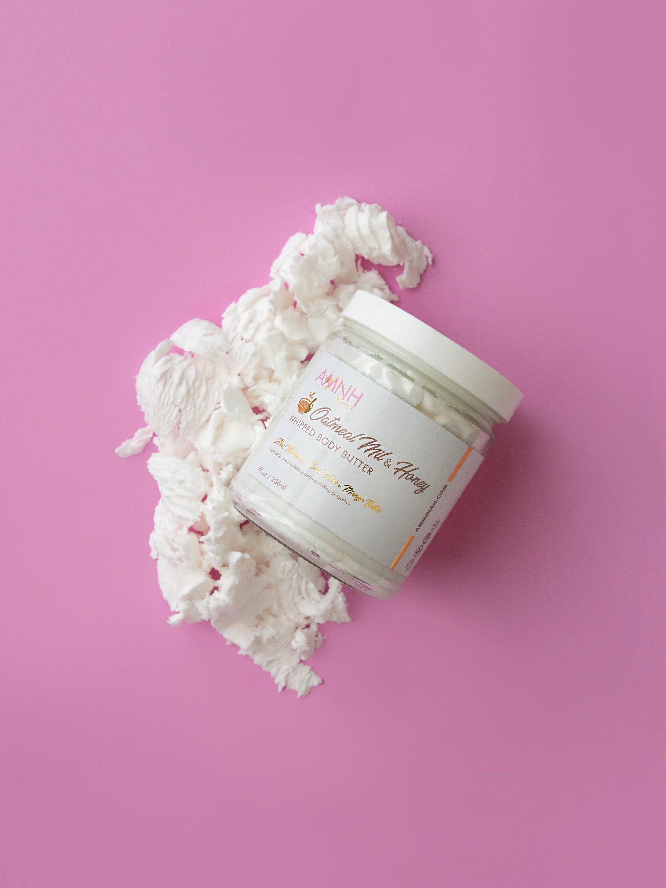 Oatmeal Milk & Honey Whipped Body Butter in clear glass jar on a soft pink background with whipped body butter texture, ultra-moisturizing natural skincare, vegan, cruelty-free, clean beauty body moisturizer by AMNH Skincare.
