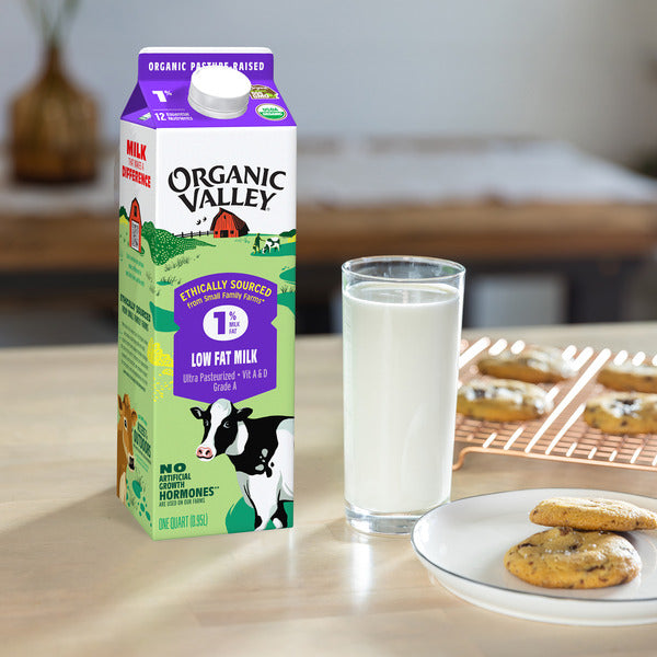 Organic Valley Organic 1% Low Fat Milk carton beside a full glass of milk and freshly baked chocolate chip cookies on a kitchen table, made with USDA Organic certified milk from pasture-raised cows and ethically sourced from small family farms, 64 fl oz carton.