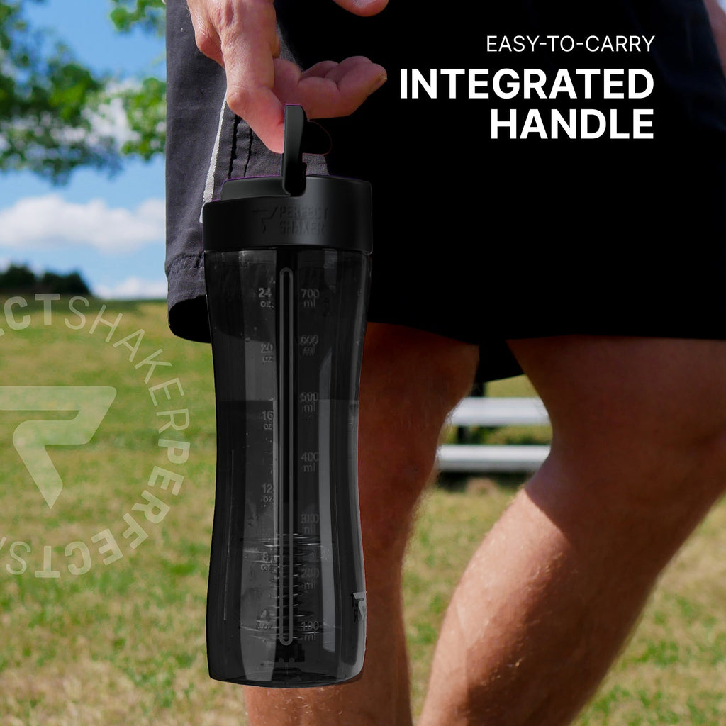A person outdoors holding a translucent black shaker bottle with an integrated handle. The bottle has white measurement markings and a black lid.
