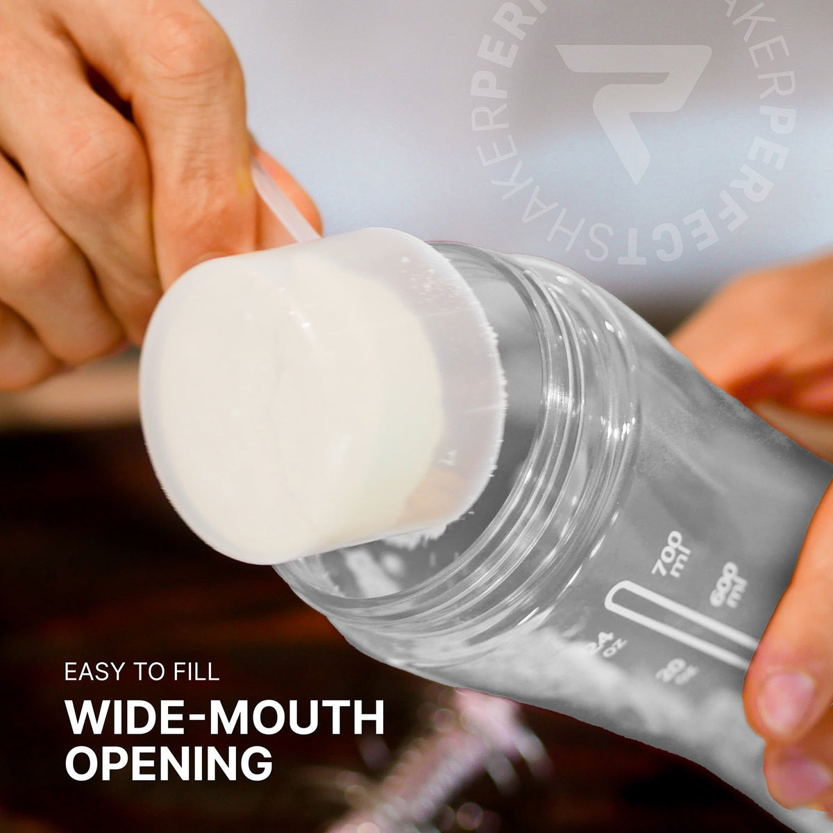 Close-up of a person's hands filling a clear powder shaker bottle with a scoop. The bottle has a wide mouth opening and visible measurement markings.