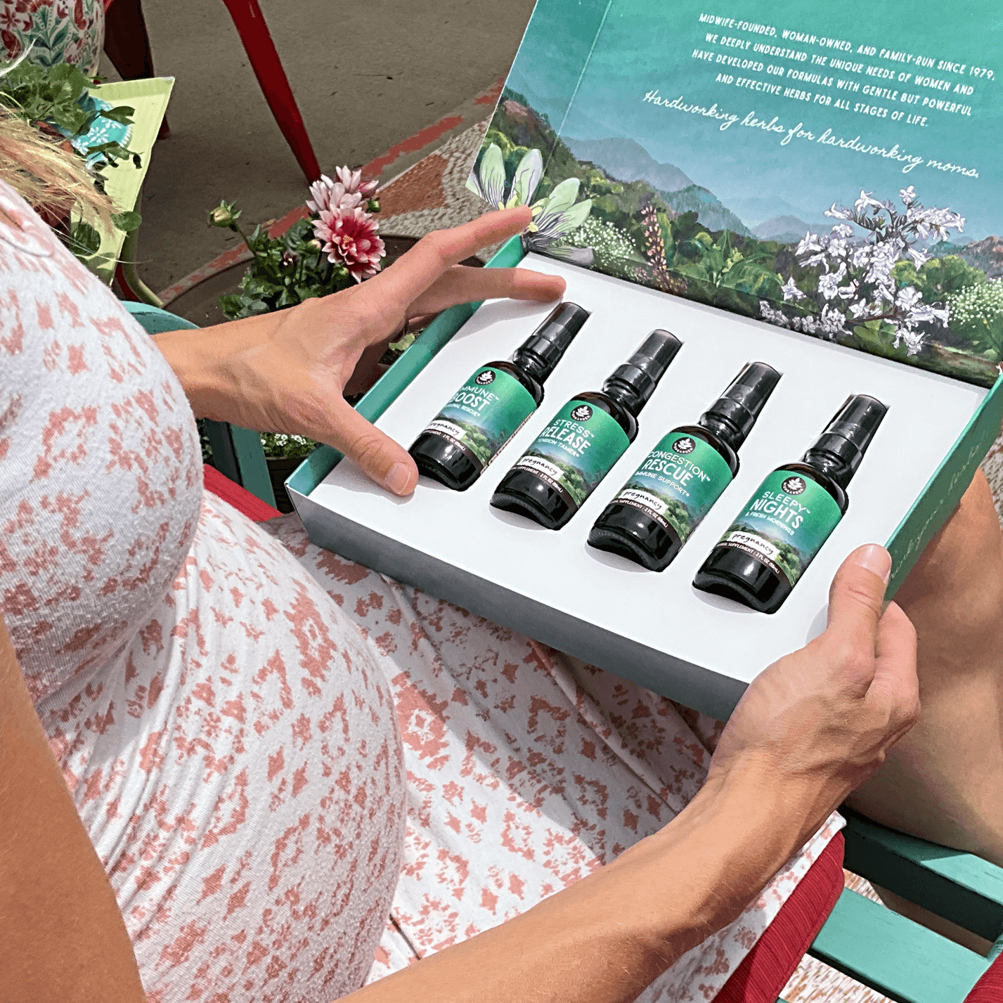 Person holding a box of green and black bottles with a scenic background. (Congestion Rescue, Immune Boost, Stress Release,  Sleepy Nights)
