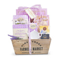 Gift basket with tea packages and a wooden box labeled 'Alde Creek Farmers Market' on a white background. Relaxing Lavender Tea Gift: Angelina’s Butter Tea Cookies, Amaretti Cookies, Snickerdoodle Cookies, Assorted Fruit Slices, Coffee Bean &amp; Tea Leaf English Breakfast Tea, Ceramic Tea Caddy, Reusable Wood Crate