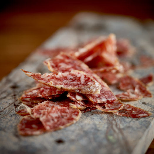 Rustic slices of premium Ibérico salchichón arranged on a weathered wooden board, highlighting rich marbling, natural texture, and traditional Spanish cured sausage craftsmanship.