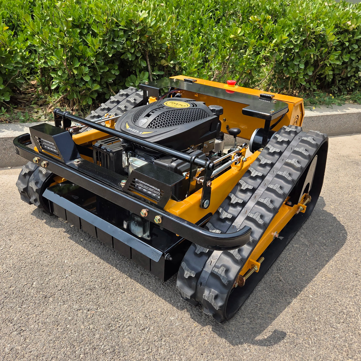 A yellow and black tracked lawn mower or garden tractor photographed outdoors on a paved surface with green shrubs in the background.