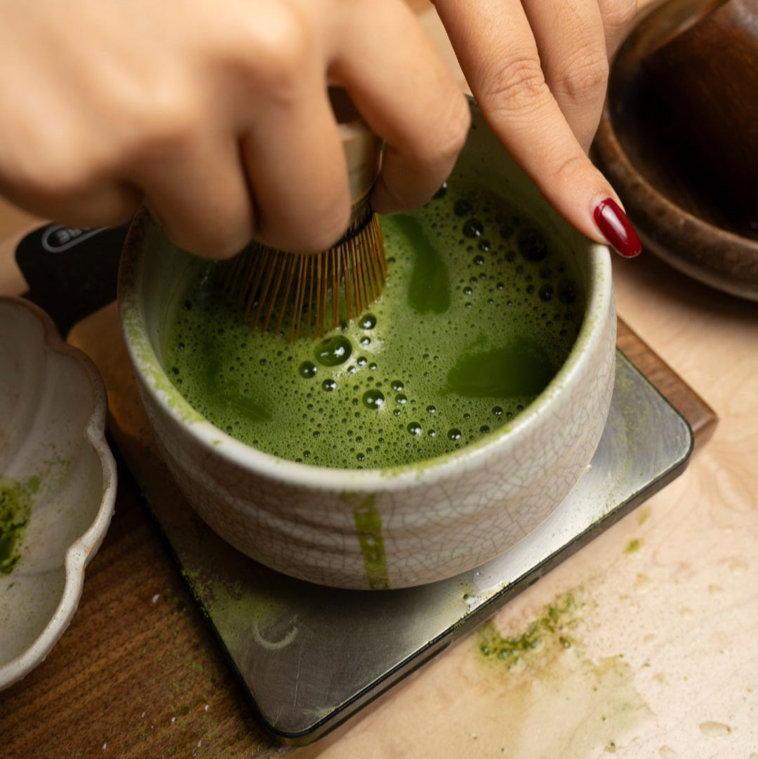 Person using a whisk to prepare matcha green tea in a ceramic bowl.