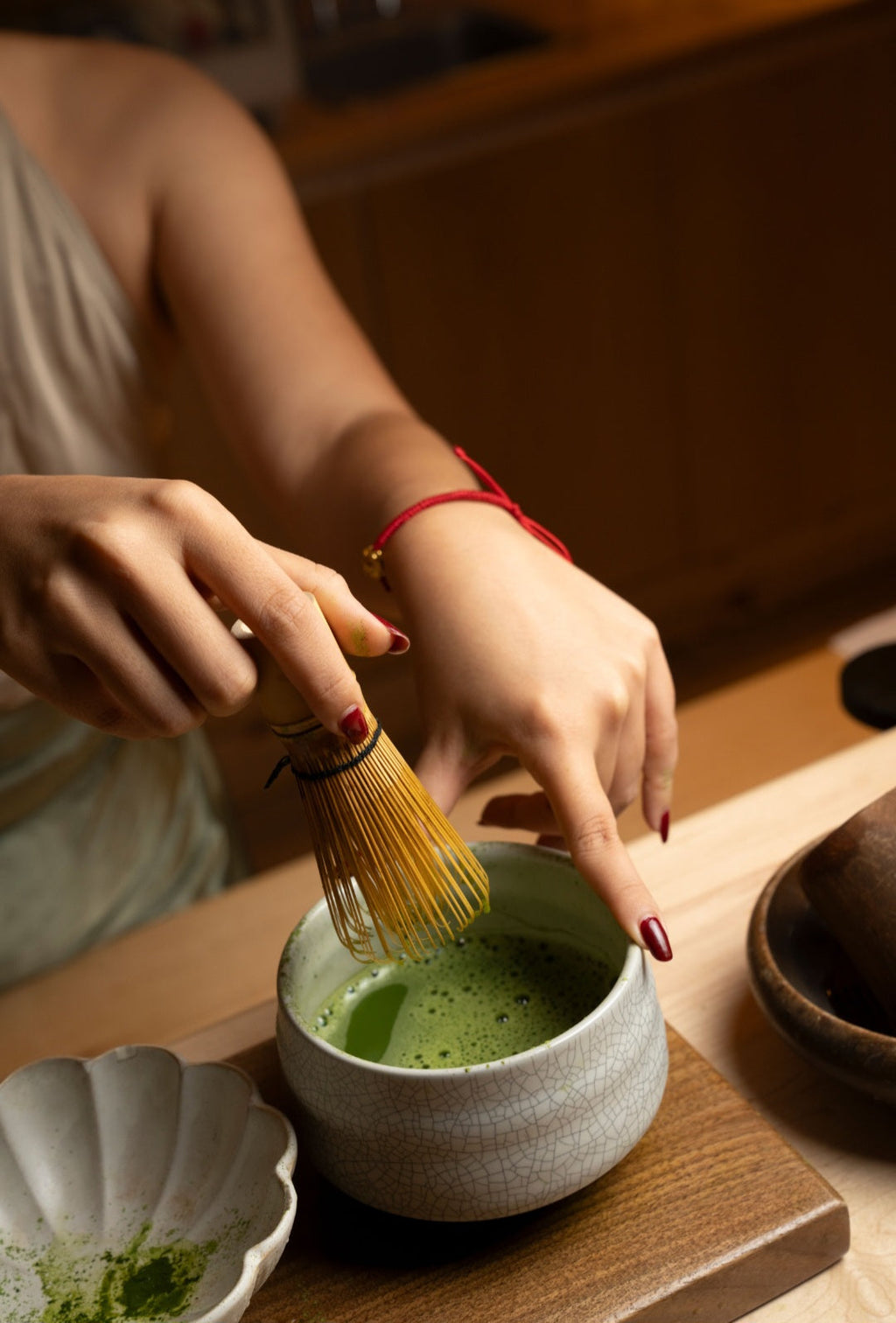 Person preparing matcha tea with a whisk on a wooden table.