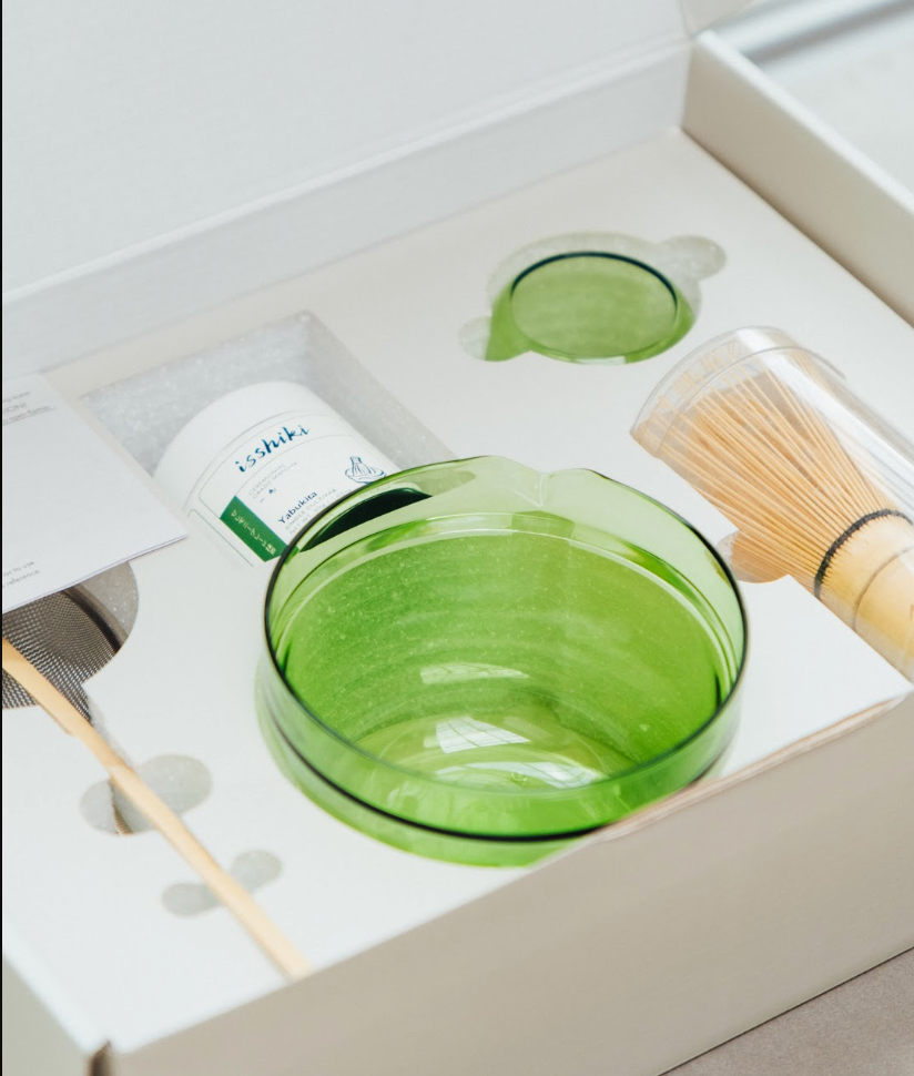 Green glass bowl with wooden whisk and green leaf-shaped item in a box
