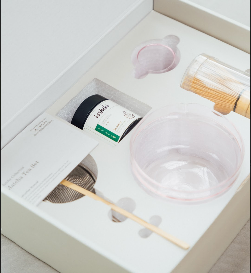 Tea-making set with a bowl, strainer, and other tools on a white surface.