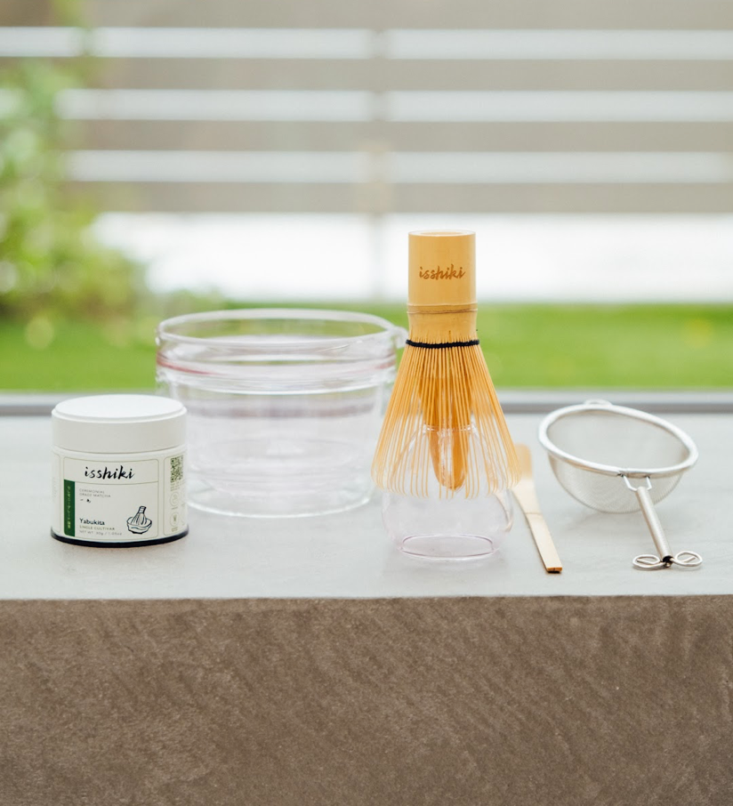 Matcha preparation set with a container, whisk, and other tools on a windowsill.
