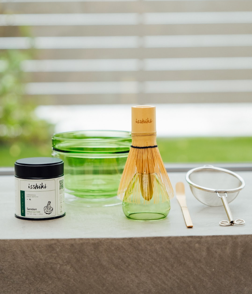 Tea-making set with green container, whisk, and other tools on a windowsill.