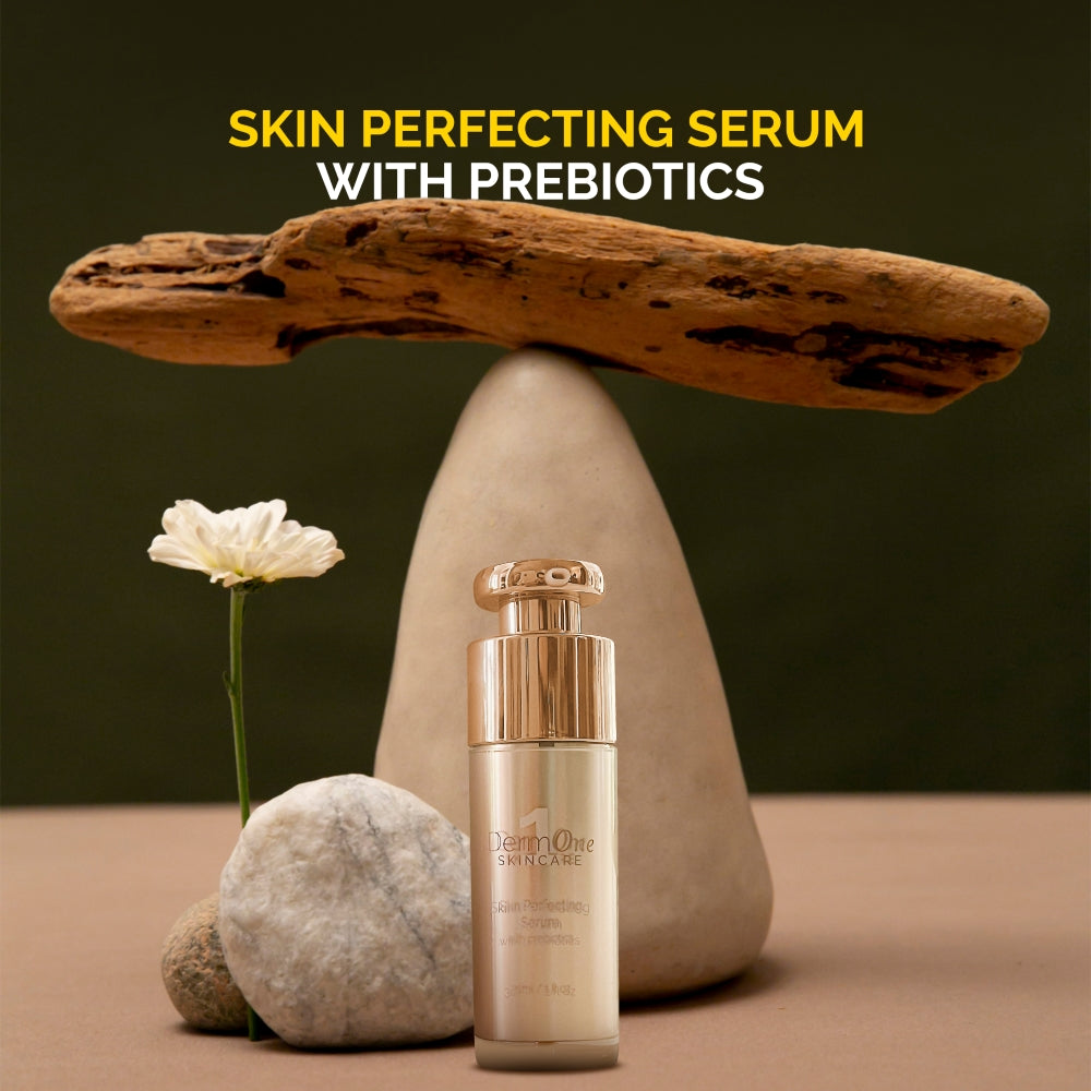 Derm #1 Skincare Skin Perfecting Serum with Prebiotics in a 1 fl oz gold pump bottle displayed with balanced stones, natural wood, and a white flower, promoting a facial serum for rosacea-prone, acne-prone, and sensitive skin.