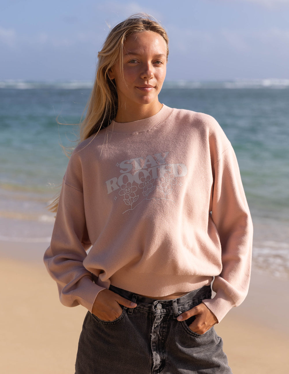 Person wearing a pink sweatshirt with text on a beach