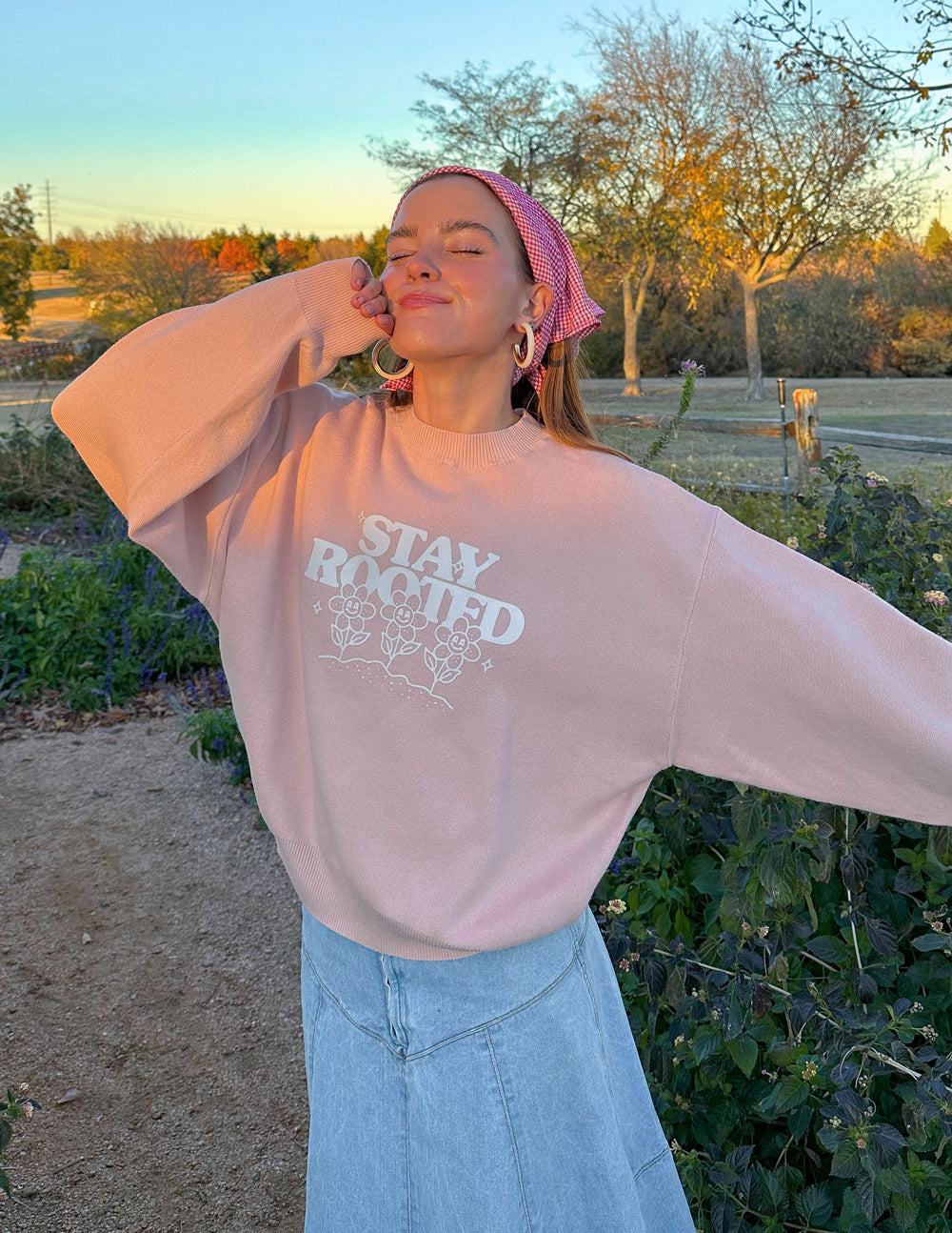 Person wearing a pink sweatshirt with 'Stay Rooted' text outdoors.