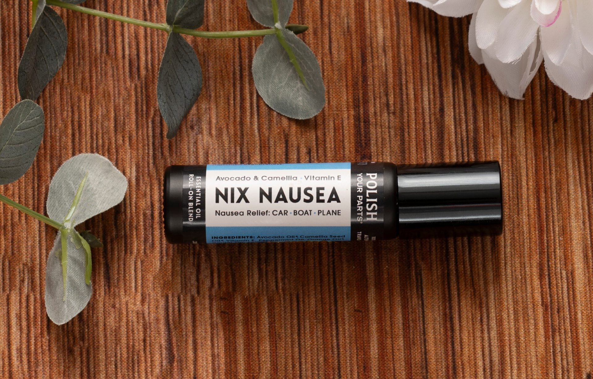 Nix Nausea rollerball for nausea relief, featuring avocado oil, camellia oil and vitamin E in a portable roll-on bottle, styled with fresh leaves and white flowers on a warm natural wood background.