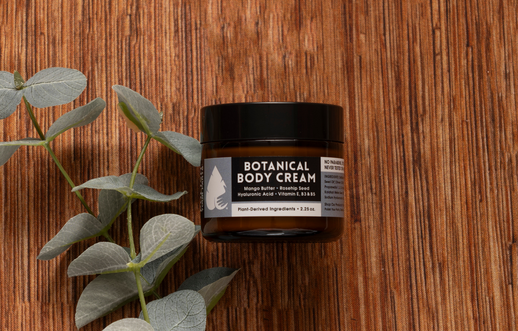 Botanical Body Cream with Mango Butter, Rosehip, Hyaluronic Acid and Vitamin E in an amber jar on a rustic wooden surface with eucalyptus leaves, natural moisturizing skincare, nourishing body cream, plant-derived ingredients, clean beauty, hydrating body care, luxury self-care, Tree of Life Grocers