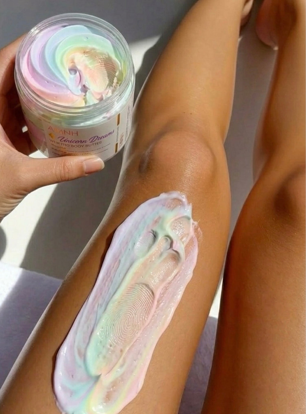 AMINNAH Unicorn Dreams Vegan Whipped Body Butter applied to skin with open jar, featuring a pastel rainbow whipped texture for deep hydration and smooth, radiant skin. Made with natural ingredients in recyclable packaging, this clean beauty, cruelty-free, vegan, paraben-free, and gluten-free body moisturizer from a female-owned brand delivers luxurious everyday body care.