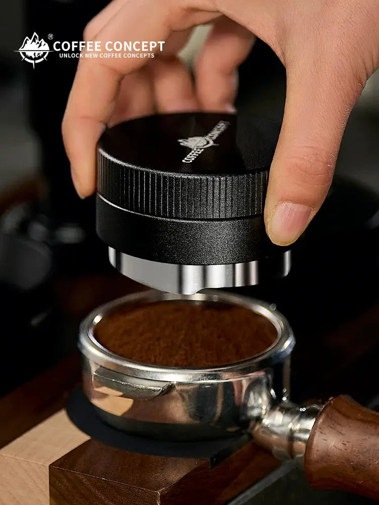 Hand using a COFFEECONCEPT stainless steel gravity espresso distributor to evenly level freshly ground coffee in a portafilter for espresso preparation.