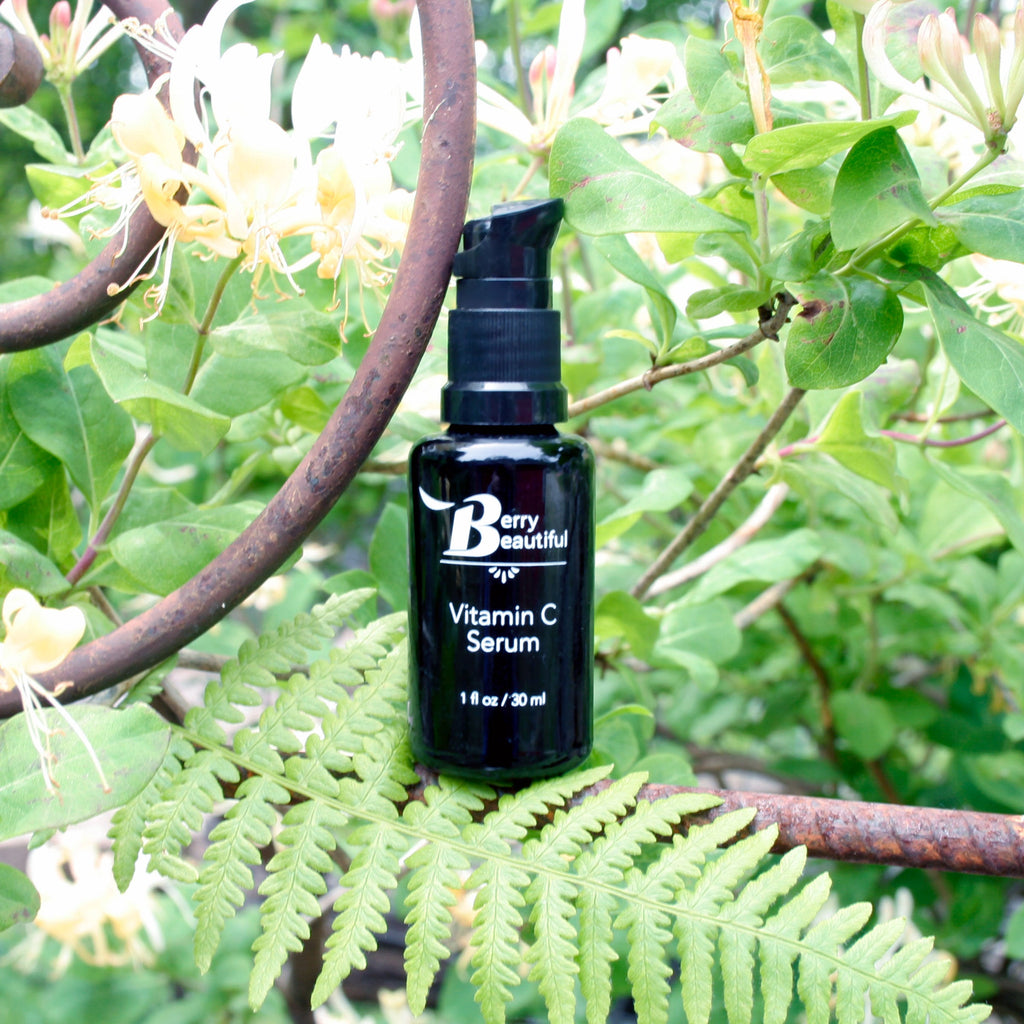 Black Vitamin C serum pump bottle labeled 'Berry Beautiful' on a green leafy background