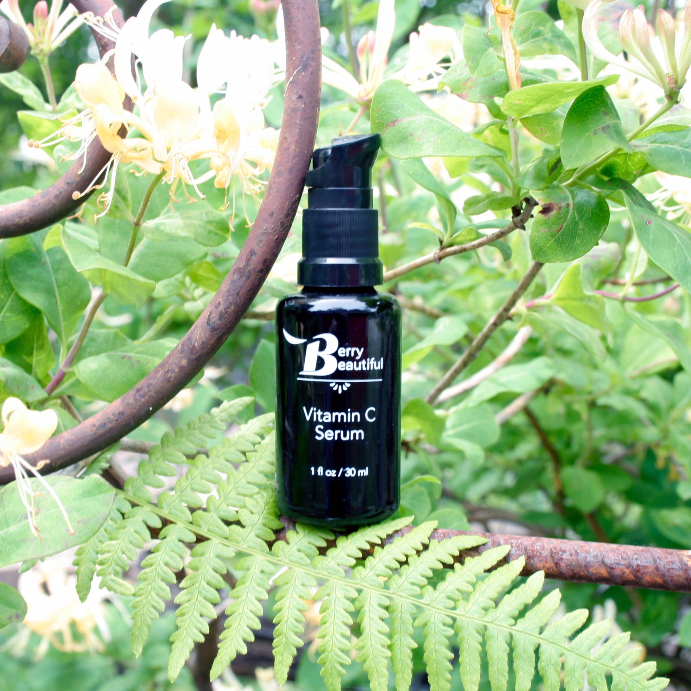 Black Vitamin C serum pump bottle labeled 'Berry Beautiful' on a green leafy background