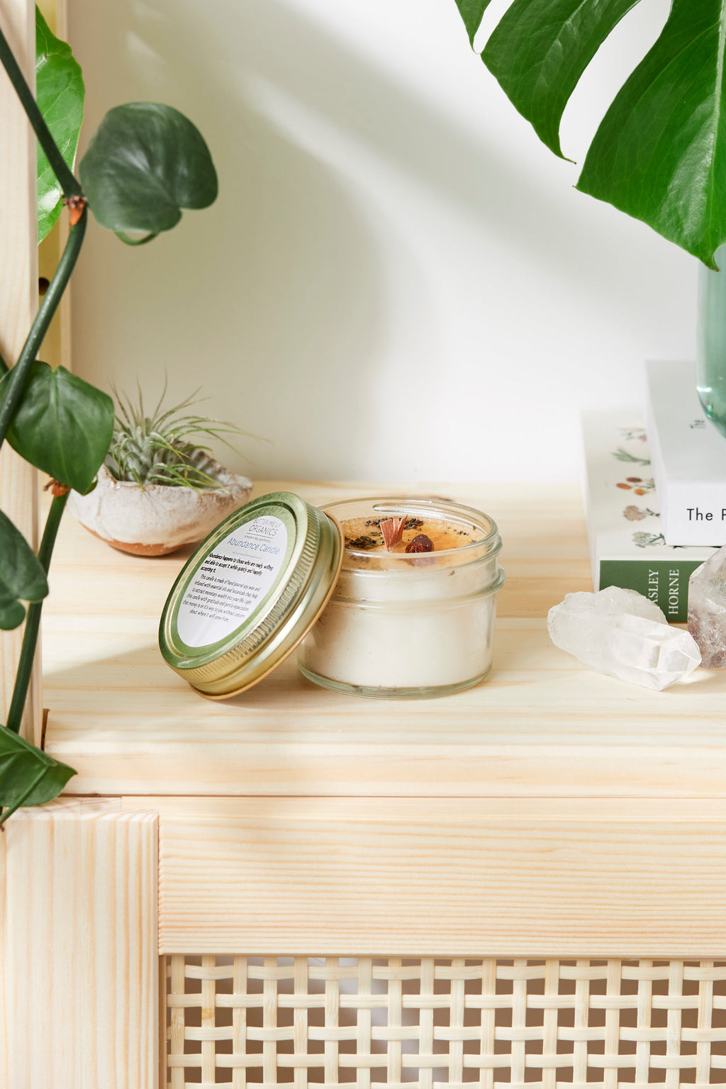 Candle and packaging on a wooden surface with plants in the background