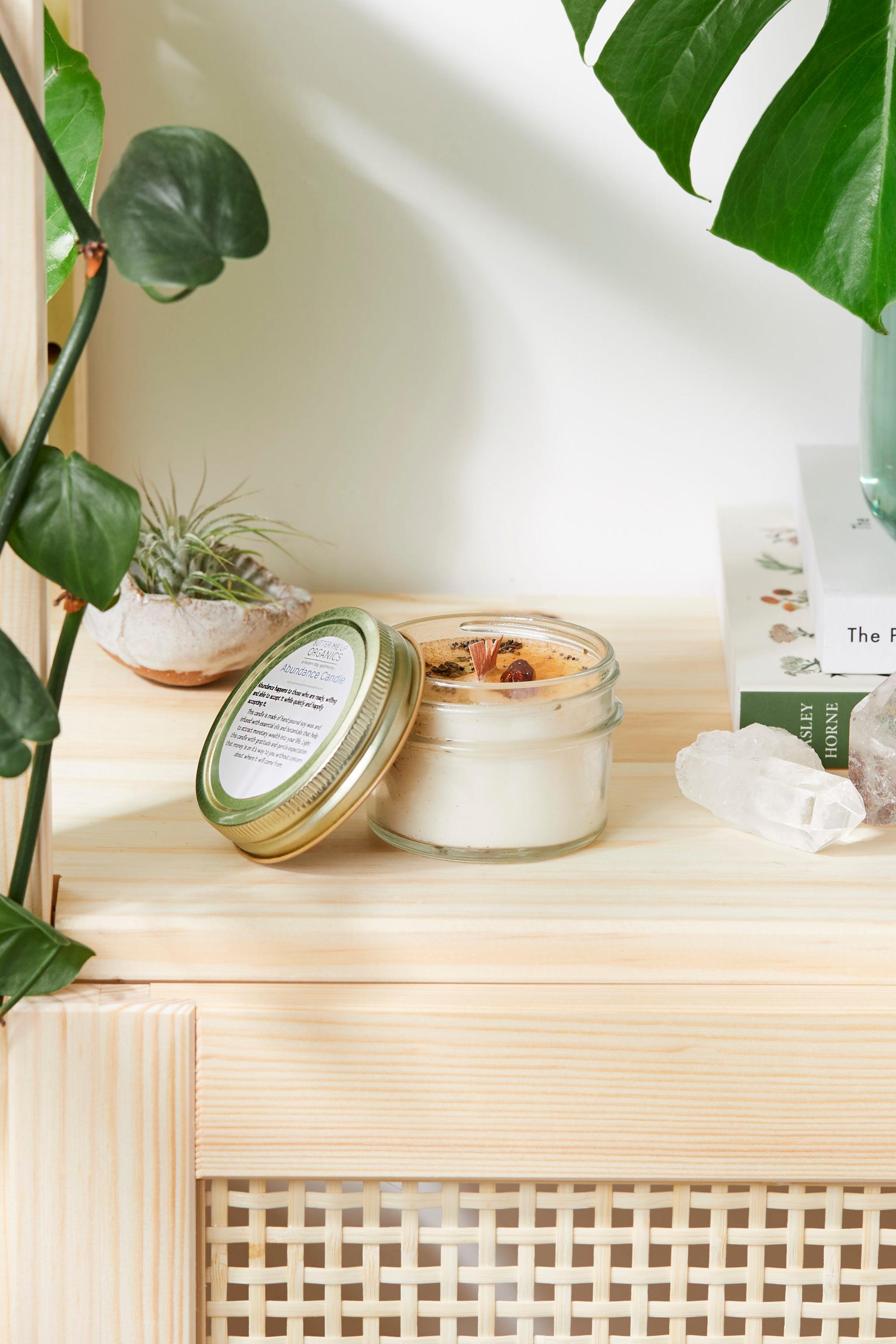 Candle and packaging on a wooden surface with plants in the background