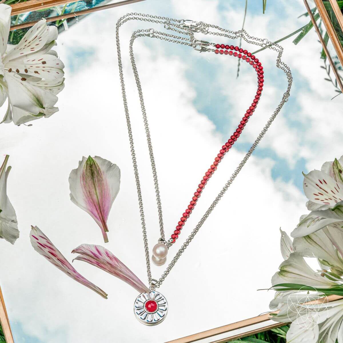 Two necklaces with pendants on a floral background. Two layer necklaces with carnelian and freshwater pearl pendants, including a red beaded necklace and a silver pendant with a red carnelian.