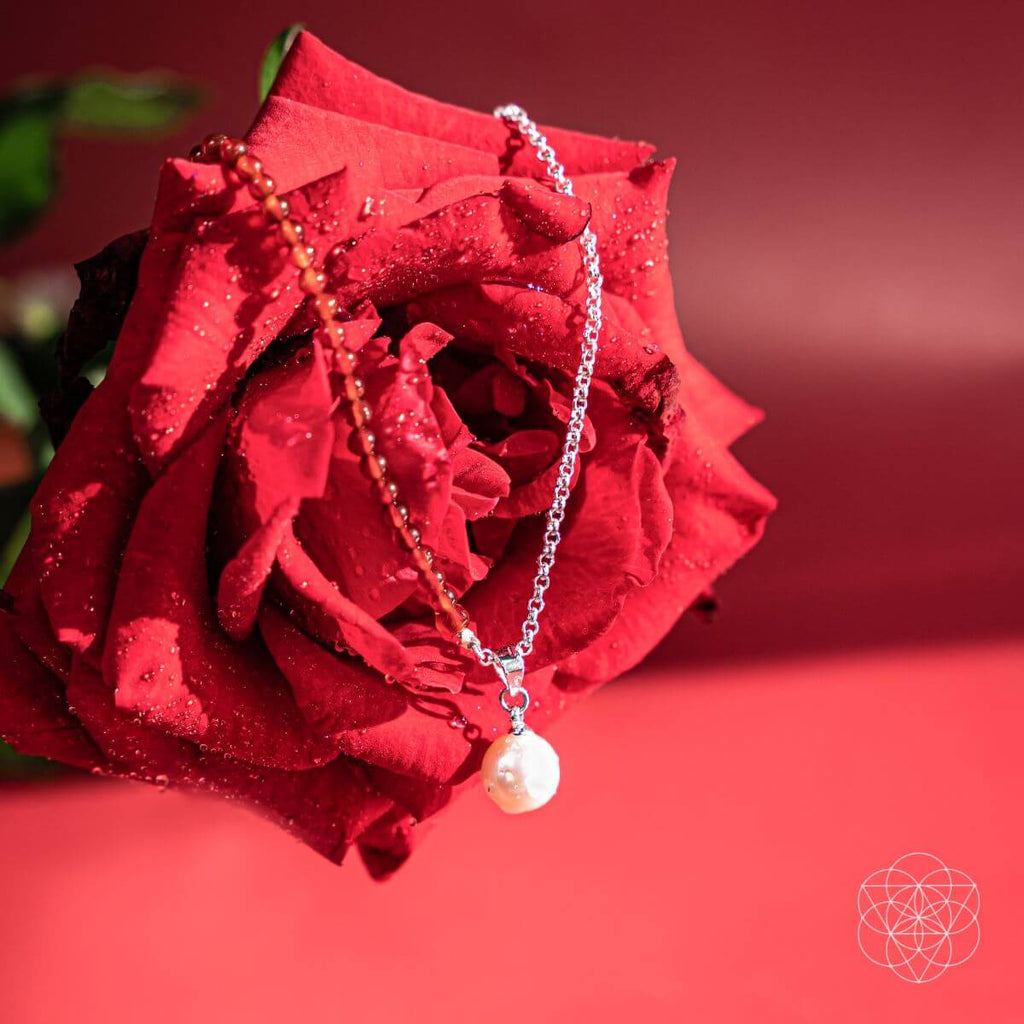 Pearl necklace draped over a red rose on a red background. Freshwater pearl pendants, including a red beaded necklace and a silver pendant with a red carnelian.