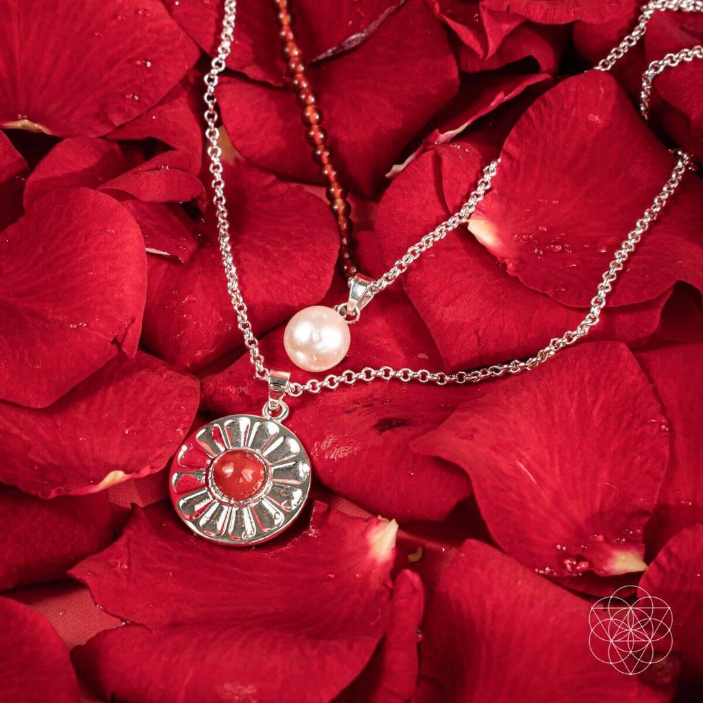 Two necklaces with pendants on red rose petals. Product display image for two layer necklaces with carnelian and freshwater pearl pendants, including a red beaded necklace and a silver pendant with a red carnelian.