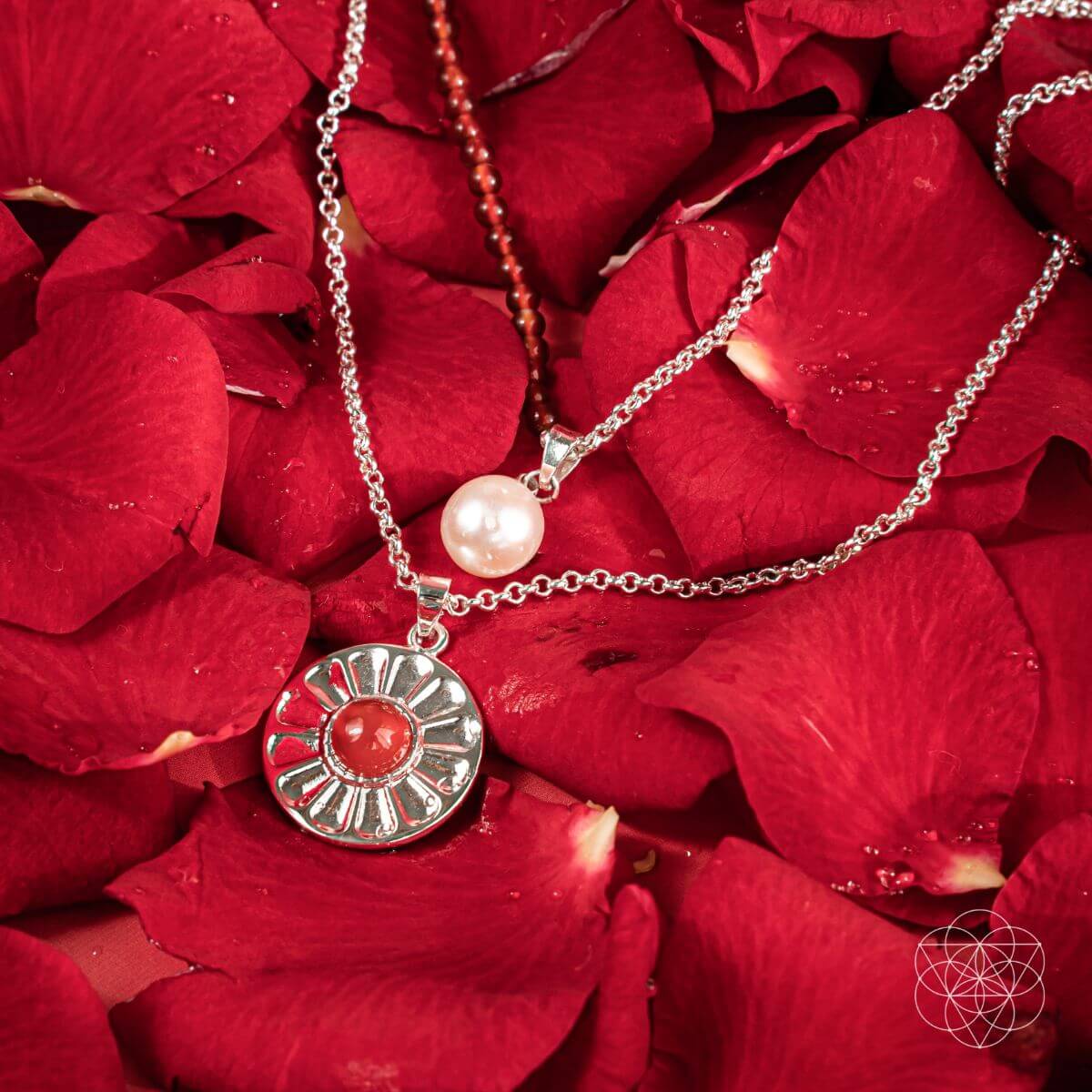 Two necklaces with pendants on red rose petals. Product display image for two layer necklaces with carnelian and freshwater pearl pendants, including a red beaded necklace and a silver pendant with a red carnelian.