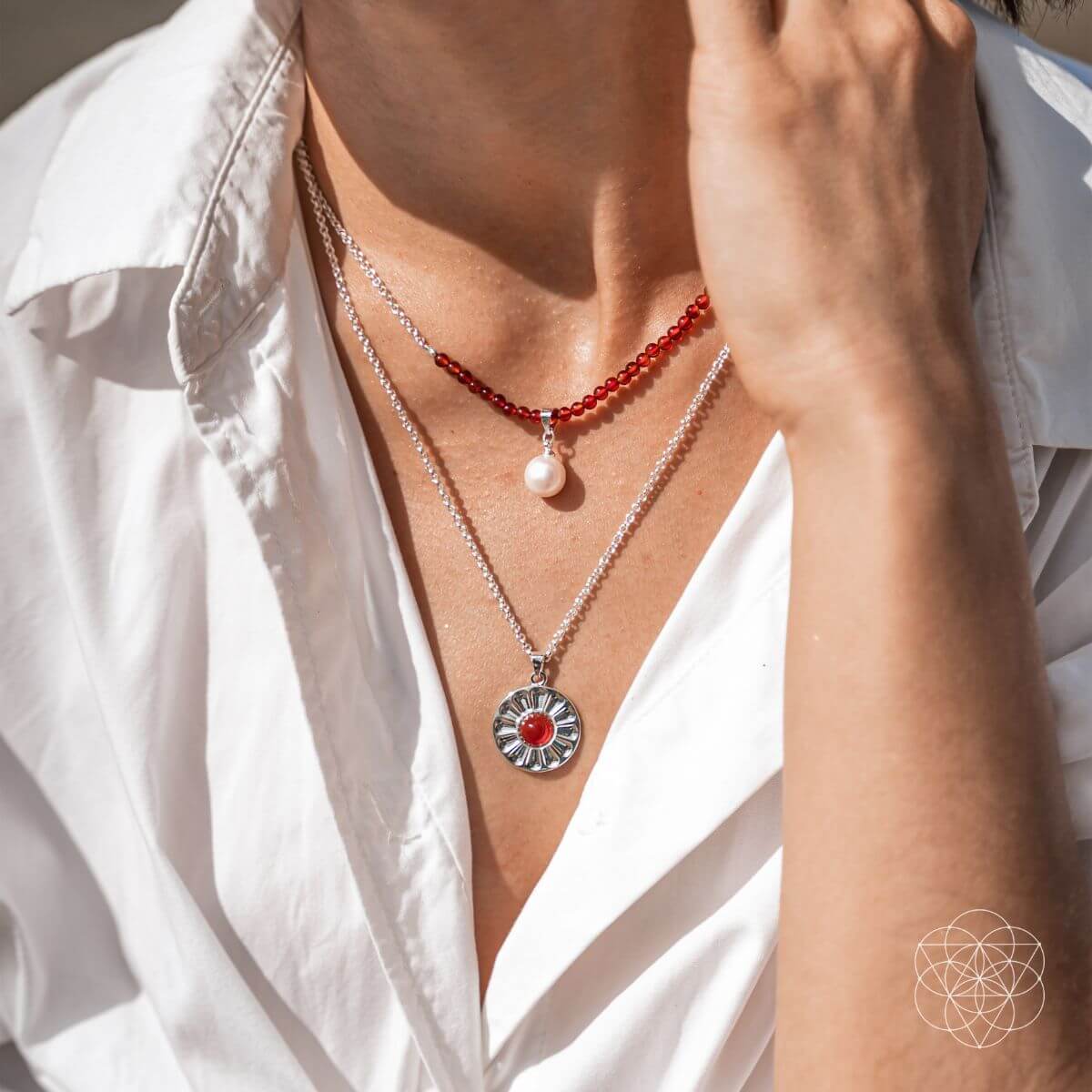 Person wearing two layer necklaces with carnelian and freshwater pearl pendants, including a red beaded necklace and a silver pendant with a red carnelian.