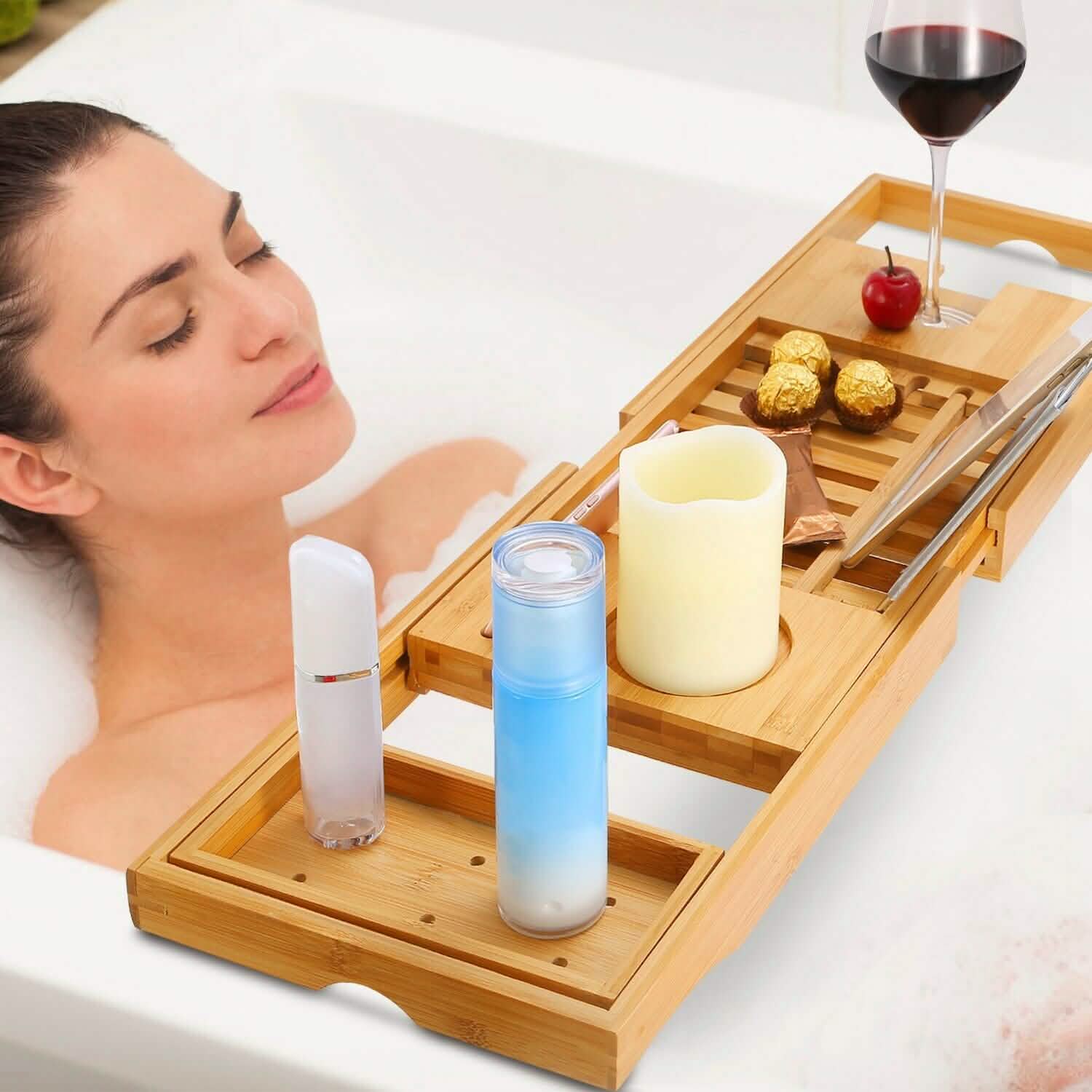 Woman relaxing in a bath with a wooden tray holding candles, drinks, and snacks. Bathtub Caddy Tray Crafted Bamboo