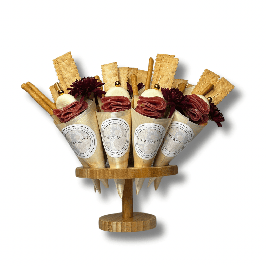 Gourmet charcuterie cones filled with cured meats, fresh mozzarella, artisan crackers, breadsticks, and floral garnish displayed on a wooden serving stand against a white background.