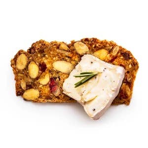 Tart cherry, cacao nib, and almond artisan crisp topped with creamy cheese and rosemary on a white background.