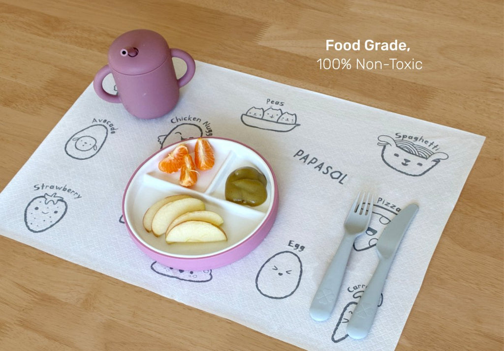 Children's placemat with cartoon illustrations, divided plate, fork, and knife on a wooden table. Baby placemats.