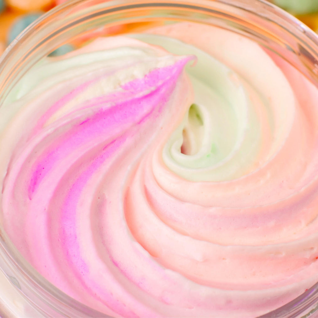Top-down close-up of AMINNAH FRUITY PEBBLEZ Whipped Body Butter featuring a fluffy pastel swirl of pink, white, peach, and light green whipped body butter inside an open jar. Rich moisturizing formula made with shea butter, mango butter, vitamin E, and essential oils to help nourish, soften, and hydrate skin. Clean Beauty, cruelty-free, vegan, made with natural ingredients, female-owned brand, made in the USA, available at Tree of Life Grocers.