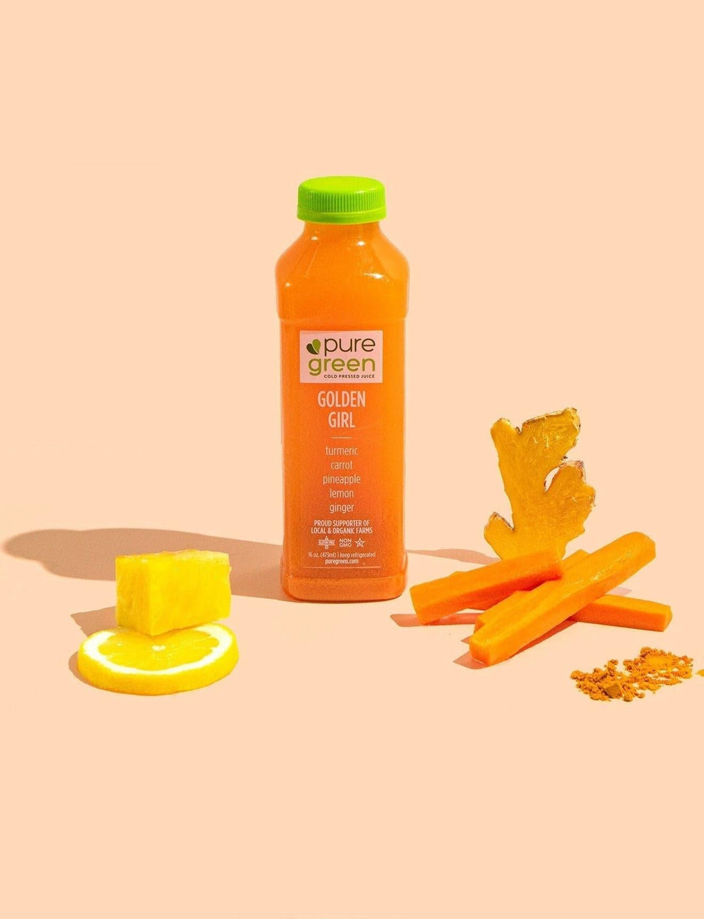 Orange juice bottle with carrots and lemon on a peach background. GOLDEN GIRL: Cold-Pressed NON-GMO Juice Drink with Pineapple, Carrot, Tumeric, Lemon, Ginger, No Added Sugar, Gluten-Free