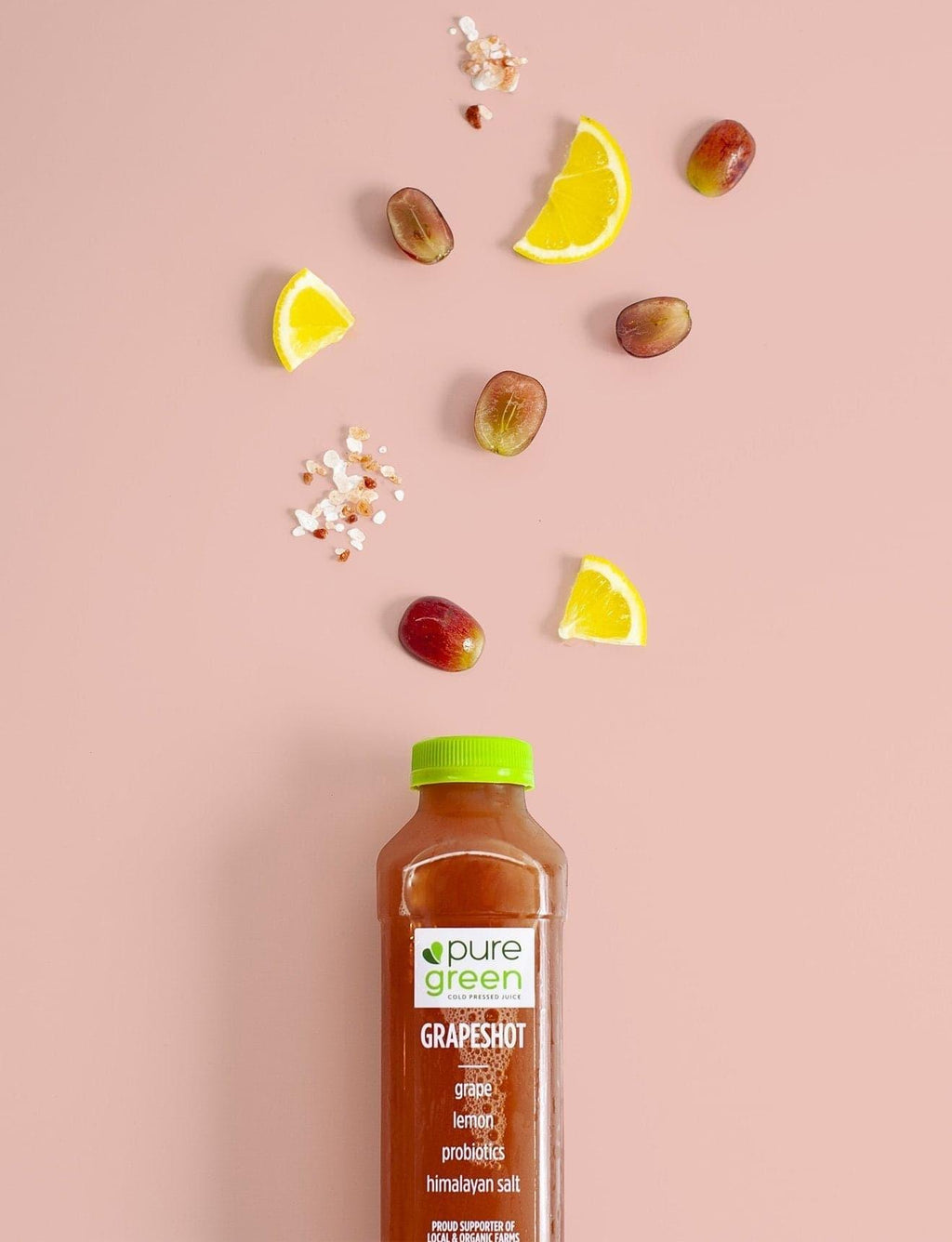 Bottle of pure green Grapeshot with grapes and lemon slices on a pink background. PURE GREEN GRAPE HYDR8 NON-GMO Antioxidant Cold-Pressed Grape Juice with Lemon, Dragonfruit, Himalayan Salt & Probiotics
