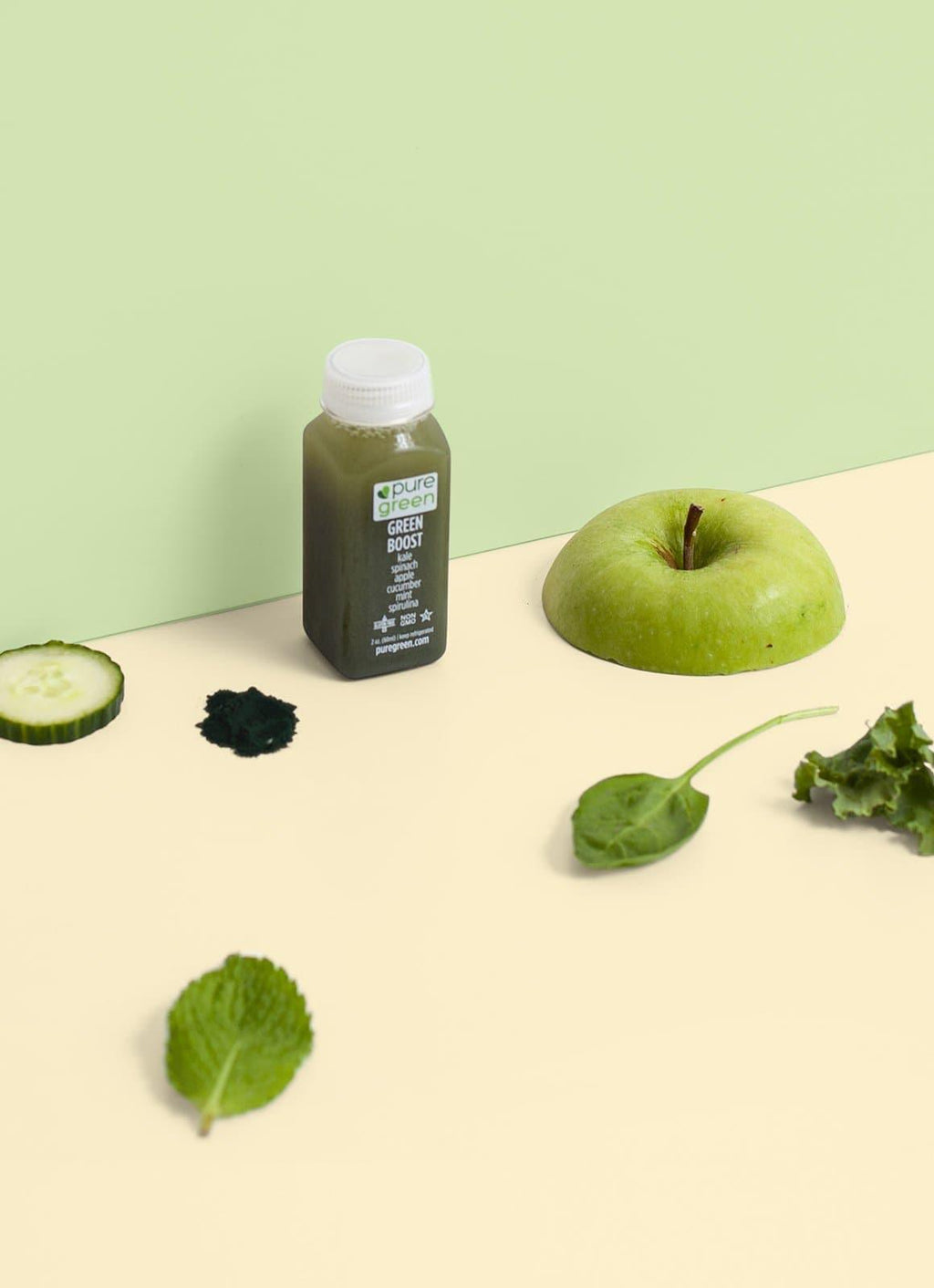 Green juice bottle with an apple, cucumber, and kale on a light green background. GREEN BOOST SHOT: Cold-Pressed NON-GMO Juice Drink with with Cucumber, Apple, Celery, Spinach, Ginger, Kale, Apple Cider, Vinegar, Spirulinal, Mint, No Added Sugar, Gluten-Free