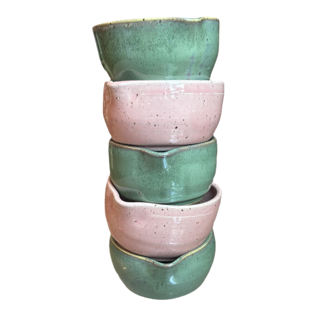 Stack of four ceramic bowls in green and pink on a white background