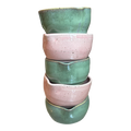 Stack of four ceramic bowls in green and pink on a white background