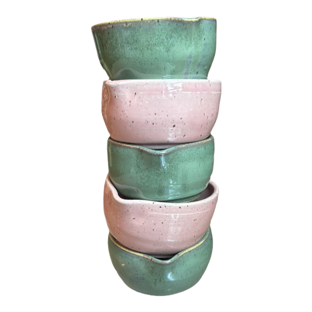 Stack of four ceramic bowls in green and pink on a white background
