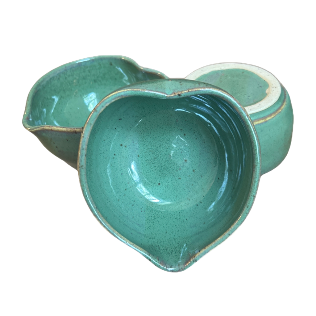 A top-down view of a handcrafted, heart-shaped ceramic matcha bowl sitting on a neutral surface, showcasing its smooth glazed finish and unique artisanal texture.