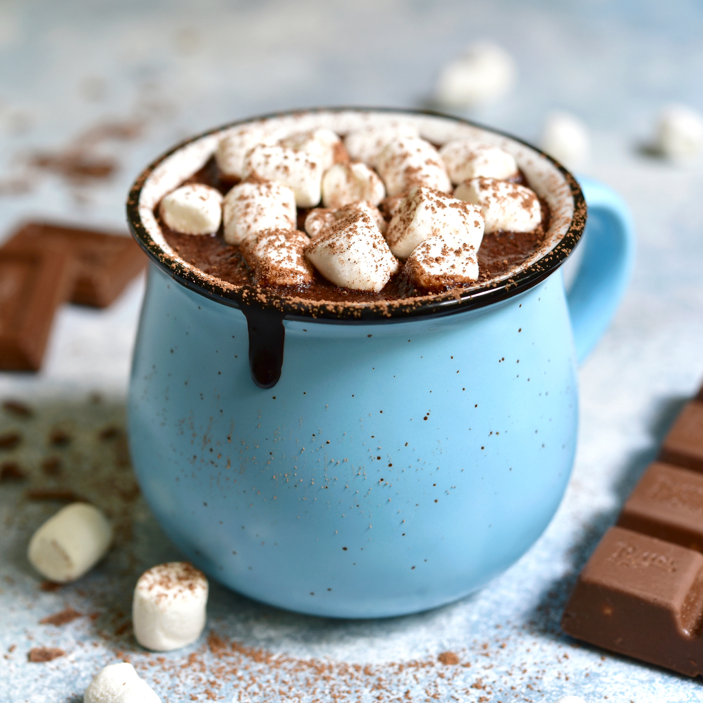 Blue mug filled with hot chocolate and marshmallows on a light blue background.
