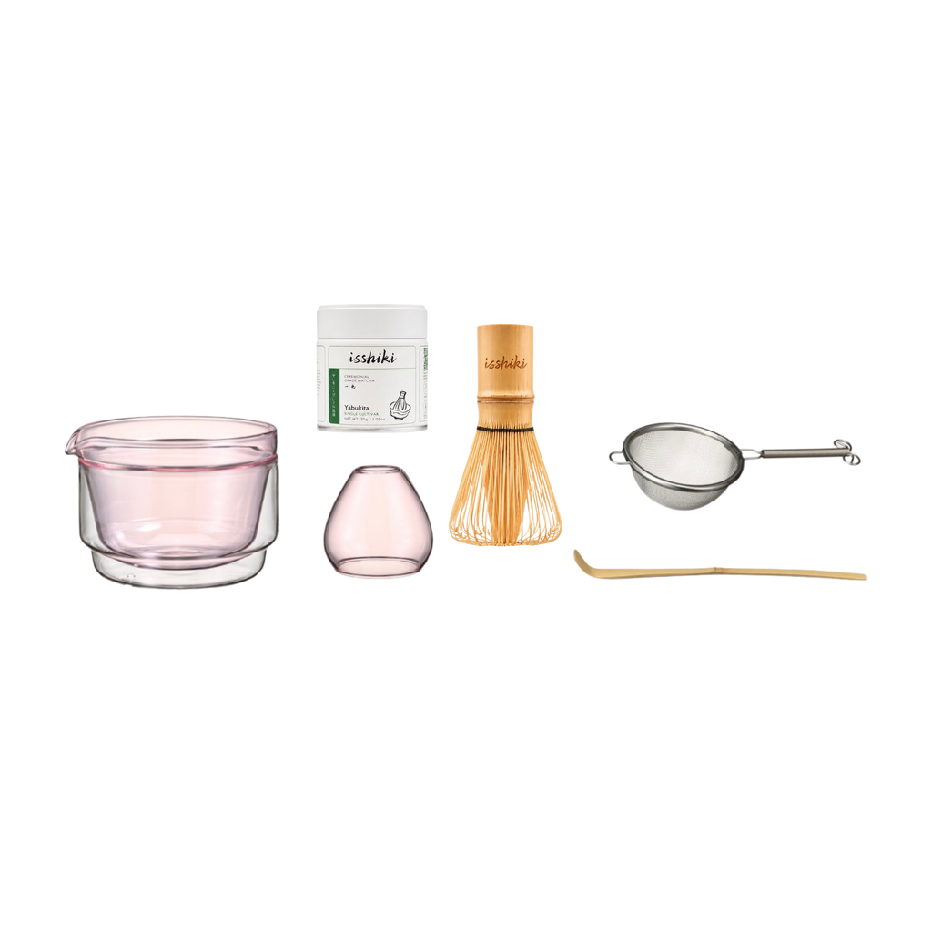 Set of tea-making tools including a pink glass, container, whisk, and other accessories on a white background.